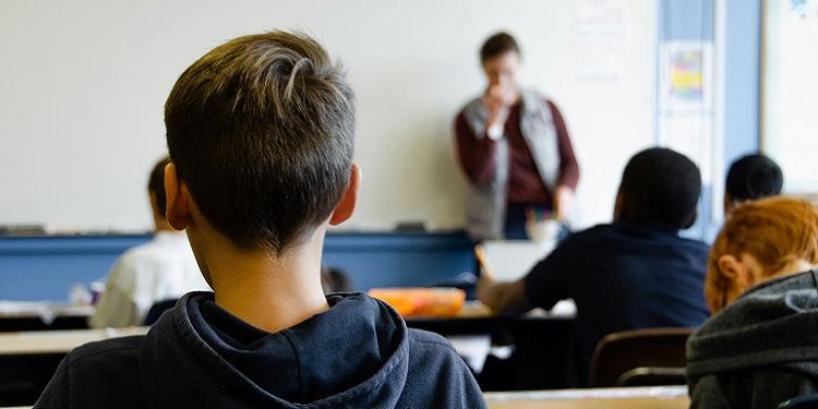 The back of a child's head in a classroom, with the teacher at the front of class